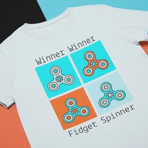 May include: White t-shirt with a graphic of four colorful fidget spinners and the text "Winner Winner Fidget Spinner".