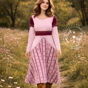 May include: A long-sleeved pink dress with a burgundy waist and sleeve accents. The dress features a patterned skirt with vertical stripes and lace detailing. The image includes the text "Pink Skies Designs".