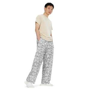 May include: A person wearing a beige t-shirt and gray and white camouflage print pants. The pants have a wide leg design and a repeating pattern of gray and white shapes. The person is standing on a white background.