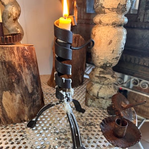 May include: A black metal candle holder with a spiral design and three legs. A white candle is burning in the holder, and wax has dripped down the sides.