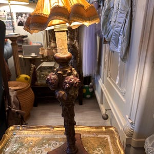 May include: An antique table lamp with a decorative base and a ruffled, golden lampshade. The lamp features a detailed, ornate design with a warm, inviting glow. The base is approximately 30 cm tall.