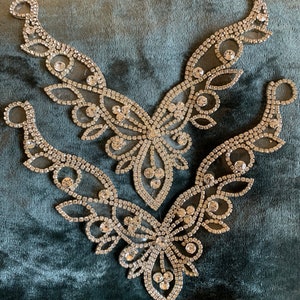 May include: Three silver rhinestone appliques with intricate floral and butterfly designs. The appliques are arranged on a teal velvet surface. Each applique features a delicate network of clear rhinestones, creating a sparkling effect.