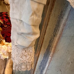 May include: A close-up of a white garment with a lace trim. The garment is hanging on a wooden surface with a blue and grey paint finish.