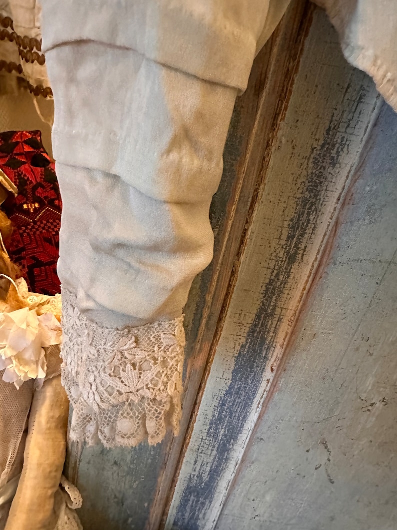 May include: A close-up of a white garment with a lace trim. The garment is hanging on a wooden surface with a blue and grey paint finish.