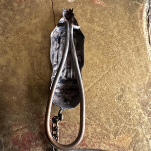 May include: Antique silver-toned religious pendant with a figure wearing a crown and cape. The pendant has a teardrop-shaped handle and a small chain. The background is a textured gold color.