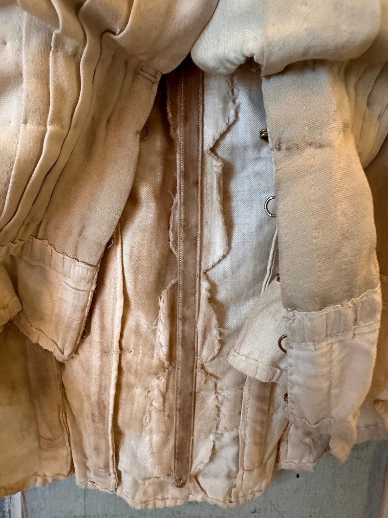 May include: A close-up of a white garment with a brown leather strap. The garment is made of a thick, woven fabric and has a frayed edge. The strap is sewn to the garment and has a decorative stitch.