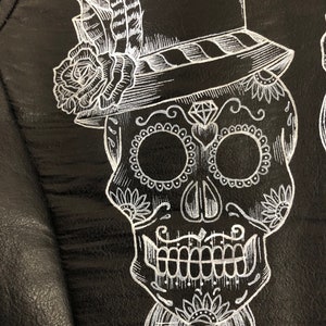 May include: A white sugar skull with a top hat, bow tie, and floral details on a black background.
