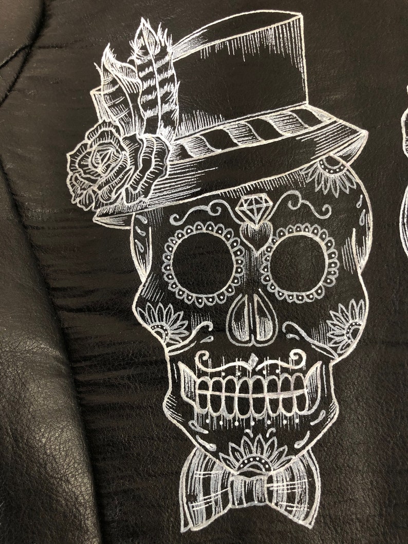 May include: A white sugar skull with a top hat, bow tie, and floral details on a black background.