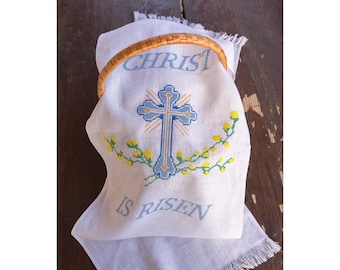 May include: White linen Easter basket liner with a blue cross and yellow flowers embroidered on it. The text "CHRIST IS RISEN" is embroidered in blue below the cross.