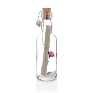 May include: A clear glass bottle with a cork stopper, containing a rolled-up scroll, a pink rose, and a small heart-shaped charm. The charm is attached to a chain that hangs from the bottle's neck. The bottle is filled with a white substance.