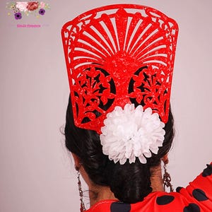 Peut inclure: Un peigne à cheveux flamenco rouge avec un motif en forme d'éventail et des découpes florales, associé à une grande fleur blanche. La femme porte une robe rouge à pois.