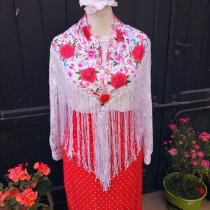 May include: White lace shawl with floral embroidery and red roses, featuring white fringe. The shawl is draped over a red polka dot skirt.