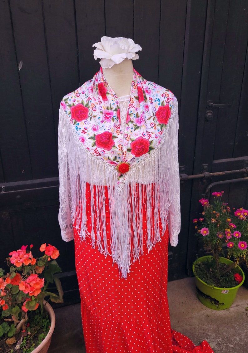 May include: White lace shawl with floral embroidery and red roses, featuring white fringe. The shawl is draped over a red polka dot skirt.