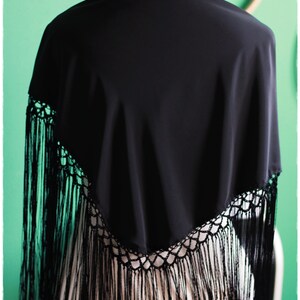 May include: A black shawl with a crocheted lace trim and long fringe. The shawl is draped over a mannequin.