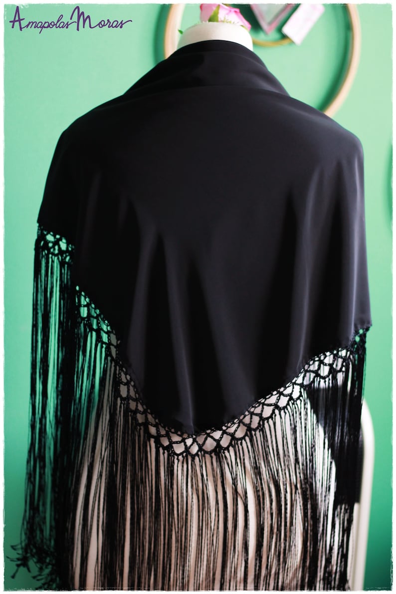 May include: A black shawl with a crocheted lace trim and long fringe. The shawl is draped over a mannequin.