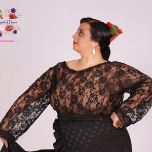 Puede incluir: Una blusa negra de encaje con mangas largas. La blusa es transparente y tiene un patrón floral. La modelo lleva una falda negra de lunares y una flor roja en el pelo.