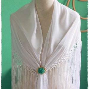 May include: White shawl with fringe and a turquoise flower brooch. The shawl is draped over a white mannequin.