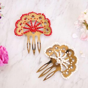 May include: Two gold hair combs with decorative fan-shaped designs. One comb is decorated with red beads and the other with white beads.