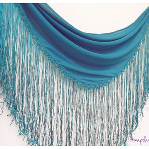 May include: A teal blue shawl with a fringe border. The shawl is made of a lightweight fabric and has a delicate, flowing drape.