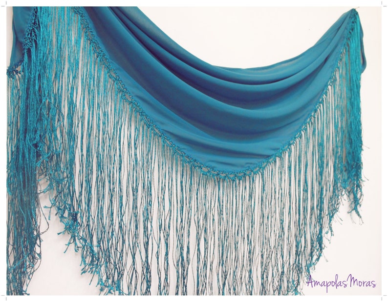 May include: A teal blue shawl with a fringe border. The shawl is made of a lightweight fabric and has a delicate, flowing drape.