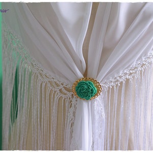May include: White shawl with a gold and green flower brooch. The shawl has fringe around the edges.
