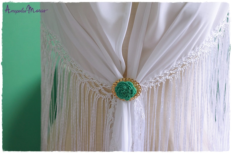 May include: White shawl with a gold and green flower brooch. The shawl has fringe around the edges.