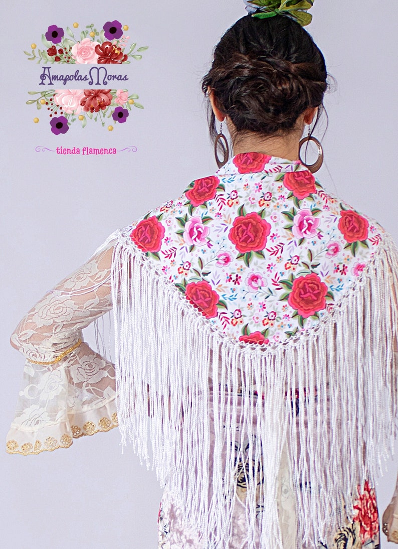 May include: White shawl with a floral pattern and white fringe. The shawl has a red, pink, and white floral design with green leaves. The shawl is worn by a person with long dark hair.