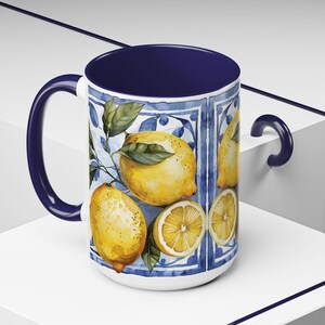 White ceramic mug with a blue rim and handle. The mug features a watercolor design of lemons and leaves on a blue and white tiled background.