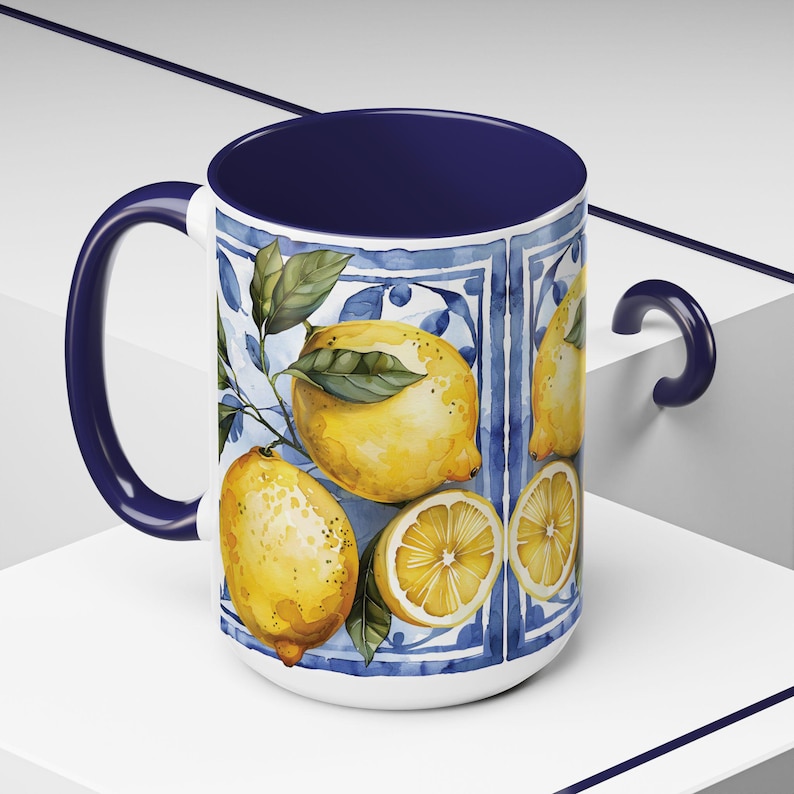 White ceramic mug with a blue rim and handle. The mug features a watercolor design of lemons and leaves on a blue and white tiled background.