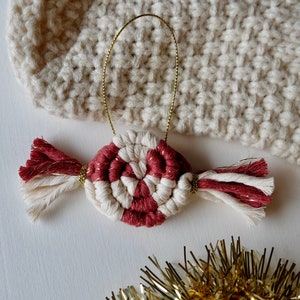 May include: A red and white candy cane ornament with gold string and tassels. The ornament is made of yarn and is a handmade Christmas decoration.