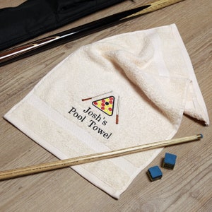 May include: A white pool towel with the text "Josh's Pool Towel" embroidered on it. The towel features a red, yellow and black pool ball rack with two brown pool cues.