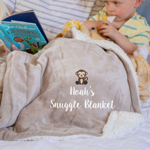 May include: A beige plush blanket with a white sherpa border. It features an embroidered monkey and the text "Noah's Snuggle Blanket".