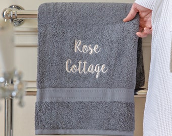 Puede incluir: Una toalla de baño gris con el texto "Rose Cottage" bordado en blanco.