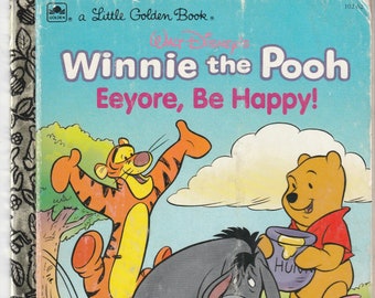 Puede incluir: Winnie de Pooh y sus amigos Tigger, Ígor y Piglet están en un campo. Tigger está saltando arriba y abajo, Ígor se ve triste y Piglet está sosteniendo un cubo de pintura. La portada del libro dice "Winnie de Pooh Ígor, ¡Sé feliz!"