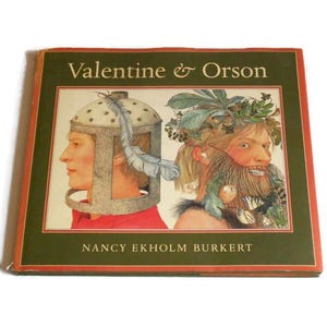 May include: A hardcover book titled Valentine & Orson by Nancy Ekholm Burkert. The cover features a green border with red edges and an illustration of two figures: one wearing a metal helmet and the other with a leafy, bearded appearance.
