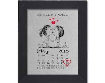 May include: Framed artwork featuring a black and white illustration of a couple kissing, with the names "ASHLEY + WILL" above. A calendar highlights May 18, 2013, with a heart. The frame is black.