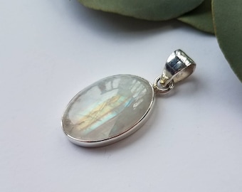 May include: Oval-shaped pendant with a polished, iridescent moonstone set in a silver bezel. The moonstone displays a play of colors, including blues and yellows. The pendant has a silver bail for a chain.