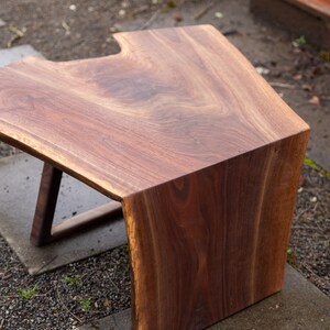 May include: A unique, live edge coffee table made from walnut wood. The table has a natural, organic shape with a smooth, polished finish. The table is supported by a simple, modern base.