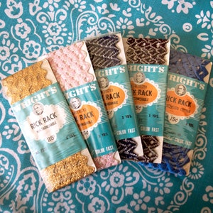 May include: Five packages of gold, pink, black, blue, and white rickrack trim. Each package has a label with the brand name "Wright's" and the text "Rick Rack" with the price and yardage listed. The packages are on a turquoise and white patterned fabric.