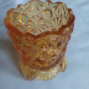 May include: A small, amber-colored glass dish with a scalloped rim and a diamond-shaped pattern. The dish has a footed base.