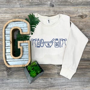 a white sweater with blue text and icons, a metal letter 'G', a potted plant, and a decorative metal object on a wooden surface.