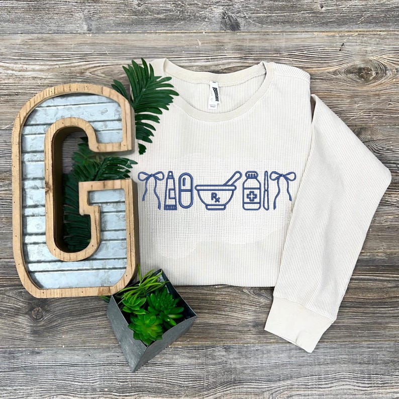 a white sweater with blue text and icons, a metal letter 'G', a potted plant, and a decorative metal object on a wooden surface.