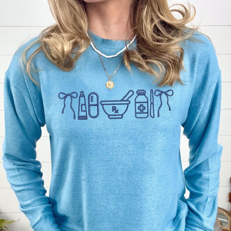 A woman wearing a blue sweater with a graphic design of medical and pharmacy-related icons printed on it.