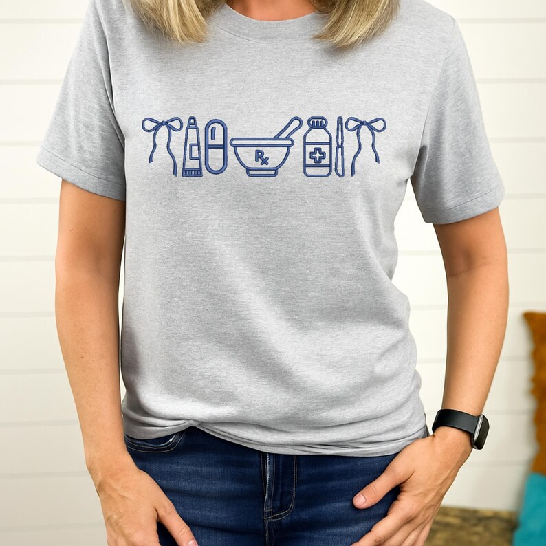 A woman wearing a gray t-shirt with a graphic design of various medical and pharmacy-related icons printed on it.