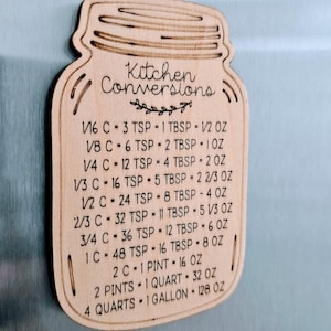 May include: Wooden kitchen conversion chart in the shape of a mason jar. The chart includes common measurements like cups, teaspoons, tablespoons, and ounces. The text "Kitchen Conversions" is at the top.