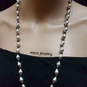 May include: A long silver necklace with faceted beads strung on black cord. The necklace is displayed on a black shirt.