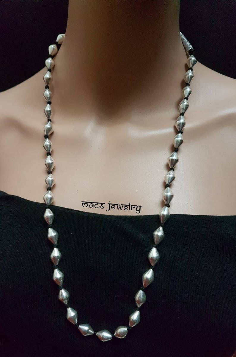 May include: A long silver necklace with faceted beads strung on black cord. The necklace is displayed on a black shirt.