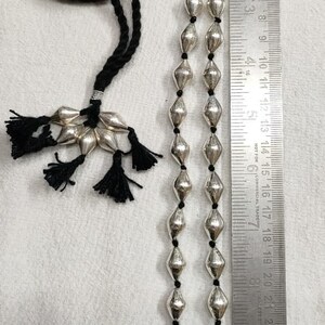 May include: A silver necklace with a black cord and silver beads. The necklace is approximately 28 inches long and has a tassel at the end.