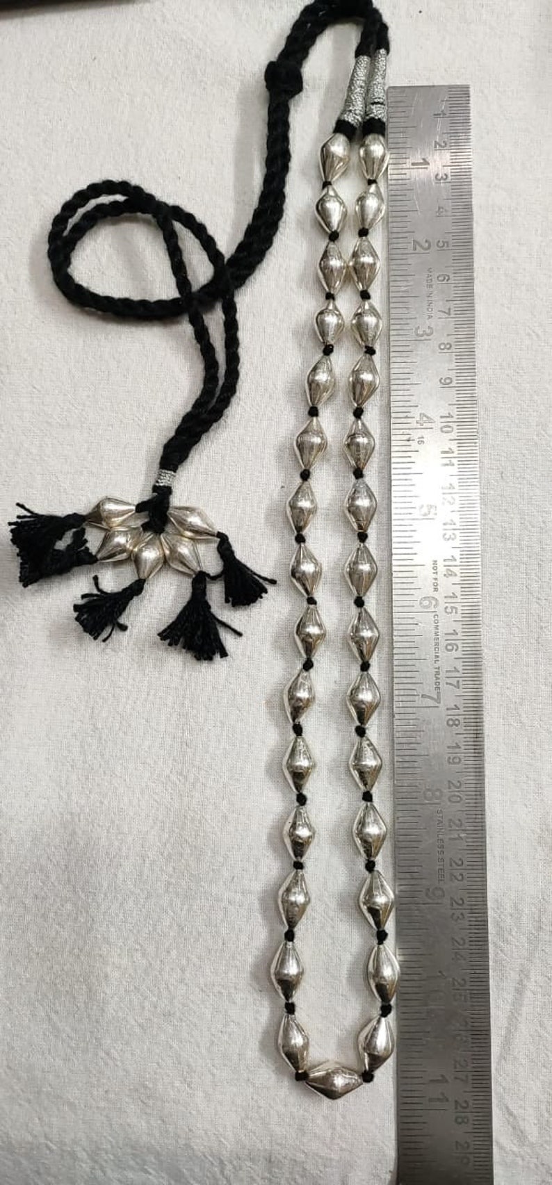 May include: A silver necklace with a black cord and silver beads. The necklace is approximately 28 inches long and has a tassel at the end.