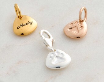 May include: Three metal charms with jump rings. One gold-tone charm is engraved with the name Marley. One rose gold-tone charm and one silver-tone charm each feature an embossed paw print design. Each charm has a smooth, rounded triangular shape.